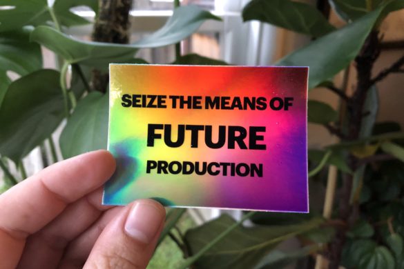 a hand holds a colorful sticket which says "Seize the means of future production" and in the background there are plants